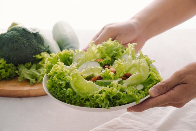 Comida de desayuno vegano verde en un tazón con lechuga, pepino, lima y almendra. Chica sujetando la placa con las manos visibles, vista superior. Comida limpia, dieta, concepto de comida vegana