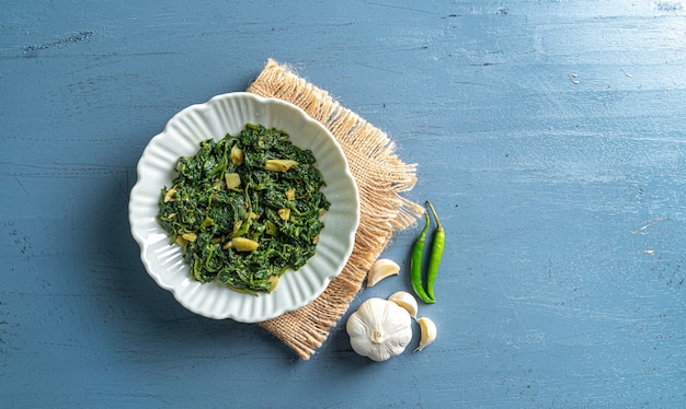 Comida de dieta cetogénica al curry de espinacas en un tazón blanco con ají con capa vintage en la vista superior de la mesa de madera azul