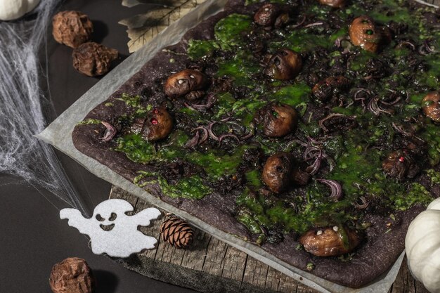 Comida do conceito de halloween. pão achatado ou pizza com tinta de lula, queijo verde, cogumelos e cebola roxa. pão dos mortos com decoração festiva, abóbora branca, velas e teia de aranha. fundo de pedra escura