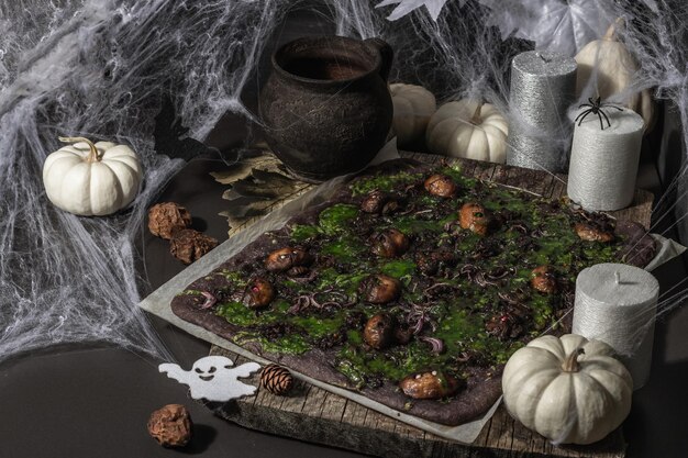 Comida do conceito de Halloween. Pão achatado ou pizza com tinta de lula, queijo verde, cogumelos e cebola roxa. Pão dos Mortos com decoração festiva, abóbora branca, velas e teia de aranha. Fundo de pedra escura