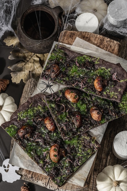 Comida do conceito de Halloween. Pão achatado ou pizza com tinta de lula, queijo verde, cogumelos e cebola roxa. Pão dos Mortos com decoração festiva, abóbora branca, velas e teia de aranha. Fundo de pedra escura