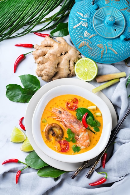 Comida e bebida, cozinha tradicional tailandesa. Tom yam kung picante, sopa azeda de tom yum com camarão, camarão, leite de coco, capim-limão e pimenta em uma tigela sobre uma mesa branca. Postura plana