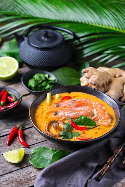 Comida e bebida, cozinha tradicional tailandesa. Tom yam kung picante, sopa azeda de tom yum com camarão, camarão, leite de coco, capim-limão e pimenta em uma tigela sobre uma mesa de madeira