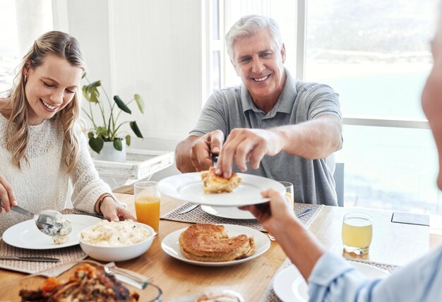 Comida em família e almoço com um idoso compartilhando uma refeição com sua filha na sala de jantar de sua casa durante uma visita Amor de aposentadoria e comendo com um idoso aposentado e parentes