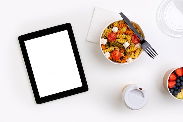 Comida em tirar caixas na mesa branca com tablet com tela em branco