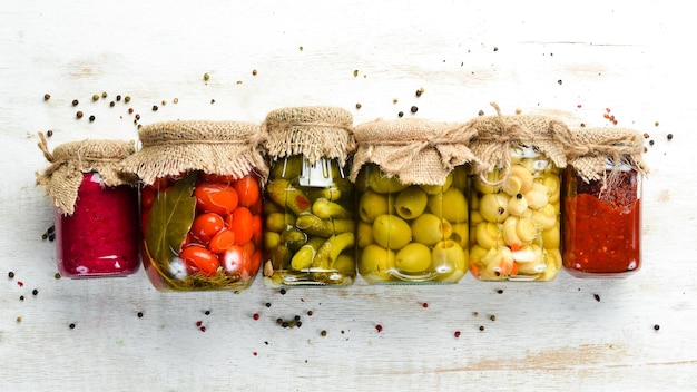 Comida enlatada en frascos de vidrio sobre fondo blanco de madera Verduras en escabeche y champiñones