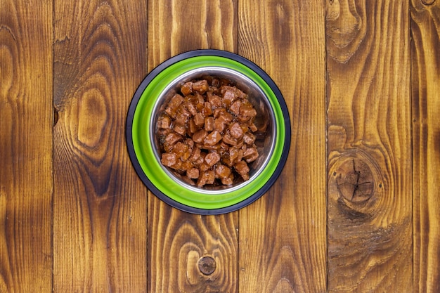 Comida enlatada para gatos o perros en un tazón de metal verde en el piso de madera Vista superior