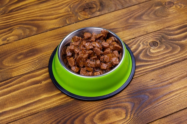 Comida enlatada para gatos o perros en un tazón de metal verde sobre un piso de madera