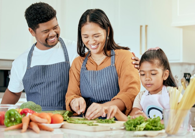 Comida familiar y cocina en la cocina para el bienestar de la salud y la nutrición con verduras y personas felices Niña de familia feliz y padres que se unen mientras preparan juntos una comida equilibrada en su hogar