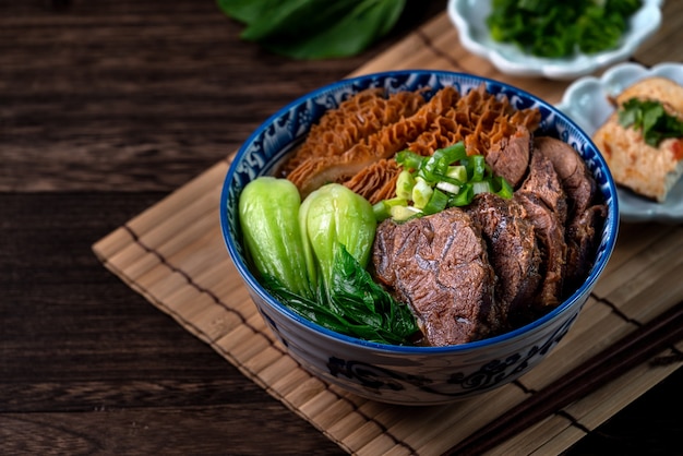 Comida famosa taiwanesa sopa de fideos de carne con pierna de ternera estofada en rodajas, callos y verduras en la mesa de madera