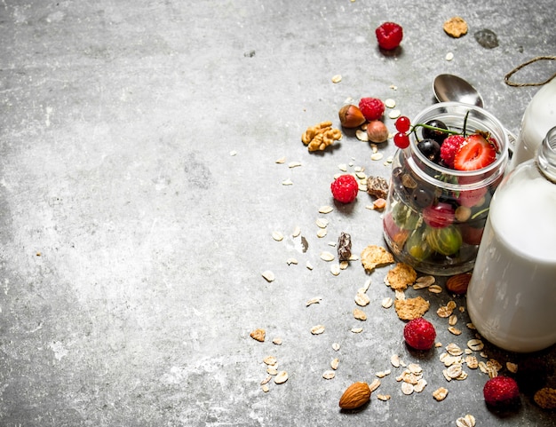 Comida fitness. Muesli con frutos rojos, nueces y leche en botellas. Sobre la mesa de piedra.