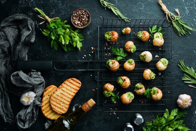 Comida francesa Caracoles al horno con salsa de pesto sobre un fondo de piedra negra Vista superior Espacio libre para el texto