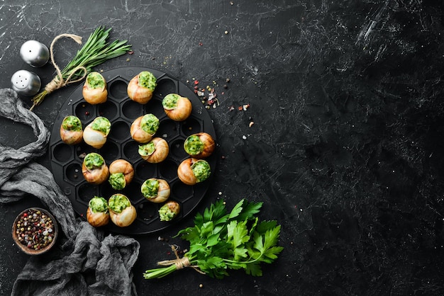 Comida francesa Caracoles al horno con salsa de pesto sobre un fondo de piedra negra Vista superior Espacio libre para el texto