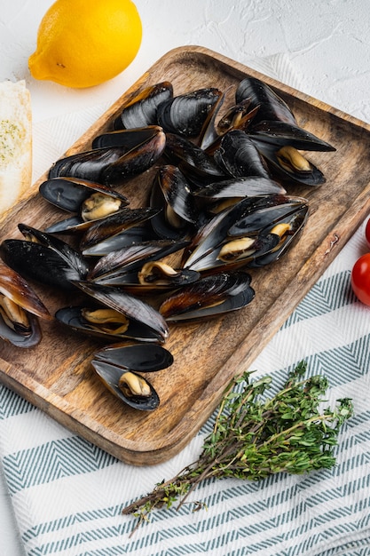 Comida francesa clásica Moules mariniere Marinara, en bandeja de madera, sobre fondo blanco.