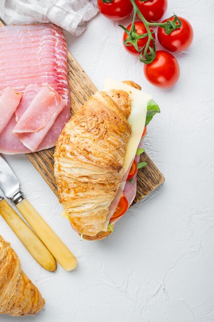 Comida francesa para el desayuno. Sándwich de croissant horneado con jamón verde y queso, con hierbas e ingredientes, sobre la mesa de piedra blanca, vista superior plana