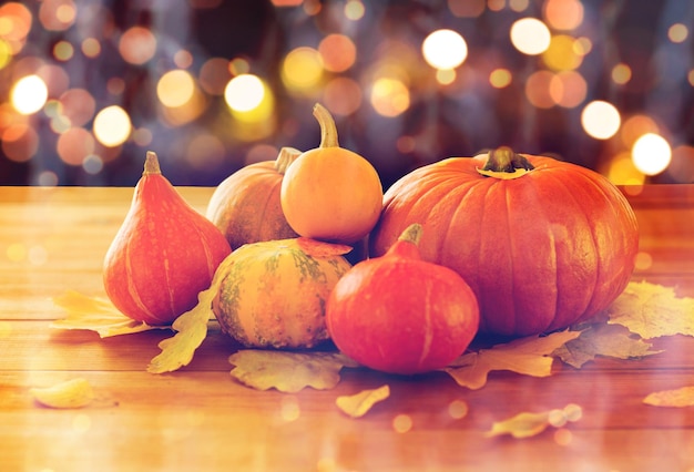 Comida, halloween, colheita, estação e conceito de outono - close-up de abóboras e folhas na mesa de madeira durante as luzes de férias