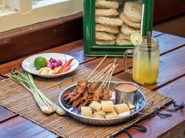 Comida de indonesia satay servida con salsa de maní y rollo de pastel de arroz