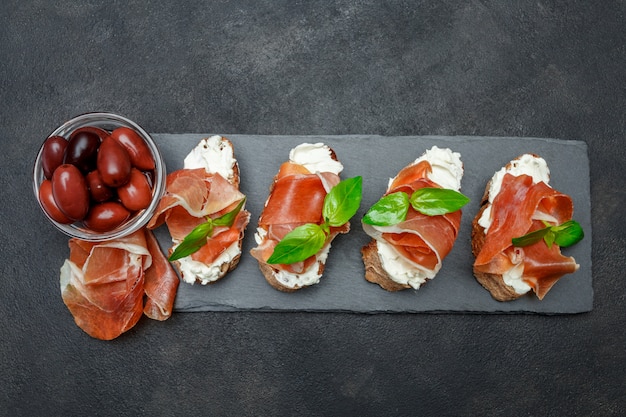 Comida italiana com azeitonas e bruschettas de presunto na placa de pedra