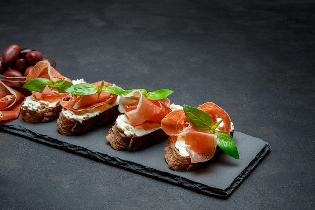 Comida italiana com azeitonas e bruschettas de presunto na placa de pedra