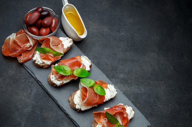 Comida italiana com azeitonas e bruschettas de presunto na placa de pedra