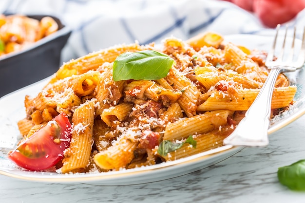 Foto comida italiana e macarrão pene com molho à bolonhesa no prato.