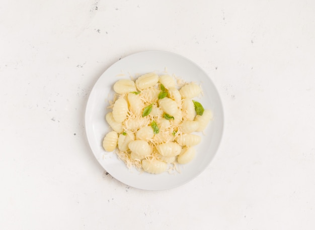 Comida italiana. Plato tradicional de ñoquis de patatas con queso y albahaca en una placa blanca.