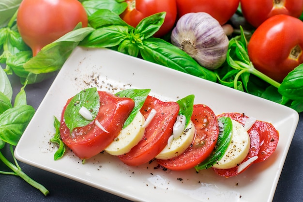 Comida italiana tradicional, fatias de tomate e mussarela e manjericão em um prato branco