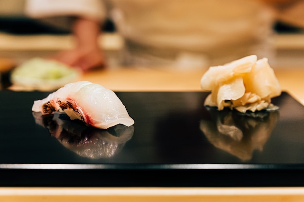 Comida japonesa de Omakase: Cierre de sushi Tai (besugo) servido en un plato negro brillante con jengibre encurtido. Comida japonesa de lujo.