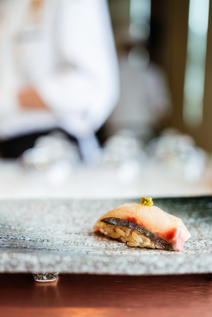 Comida japonesa Omakase Shima Aji Sushi con wasabi fresco servido a mano en un plato de piedra negra.