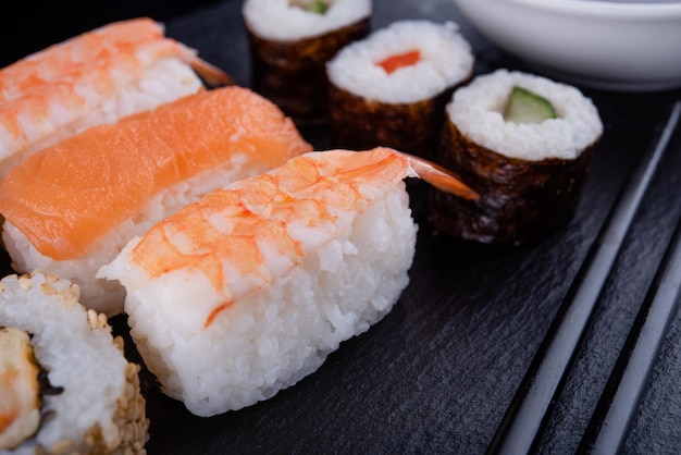 comida japonesa con rollos de sushi con camarones de atún salmón con palillos negros sobre fondo negro