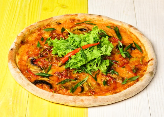 Comida para llevar con bordes crujientes. Pizza picante con ensalada en el medio. Menú de restaurante y concepto de cocina italiana. Pizza con salchichas, champiñones y cebollas verdes sobre fondo de madera amarilla.