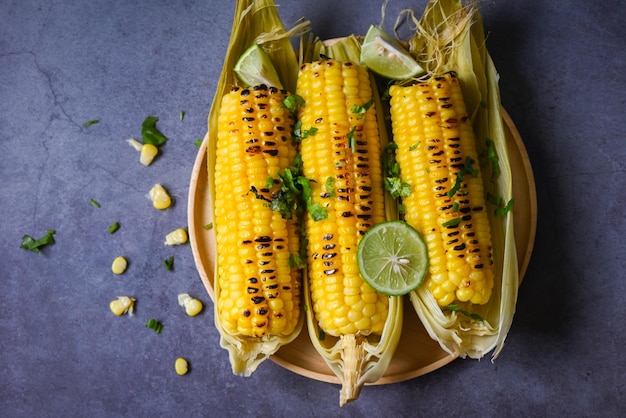 Comida de maíz dulce con lima y cilantro, maíz dulce cocinado en el fondo de un plato, mazorcas de maíz maduras, maíz dulce a la parrilla para comida, cena vegana o merienda, vista superior