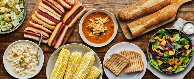 Comida de mesa con perritos calientes, queso a la parrilla, sopa y ensalada en composición plana