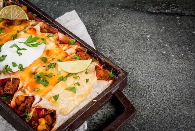 Comida mexicana. Culinária da América do Sul. Prato tradicional de enchiladas de carne picante com milho, feijão, tomate. Em uma assadeira, em uma pedra negra.