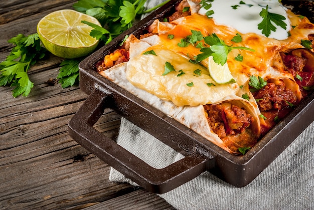 Comida mexicana. culinária da américa do sul. prato tradicional de enchiladas de carne picante com milho, feijão, tomate. em uma assadeira, sobre fundo de madeira rústica velha. copie o espaço