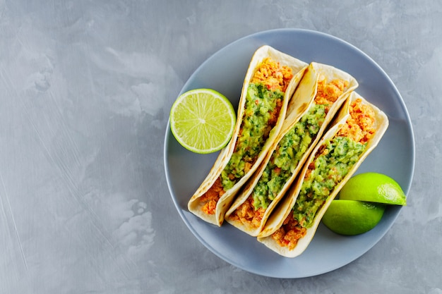 Comida mexicana. Tacos con carne picada frita y guacamole en una placa gris. Tacos mexicanos y rodajas de limón sobre un fondo gris. Copie el espacio. Vista superior