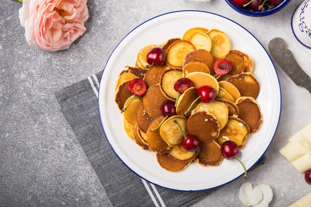 Comida de moda, mini panqueques de cereales con cereza en un tazón sobre la mesa, fondo de cemento gris.