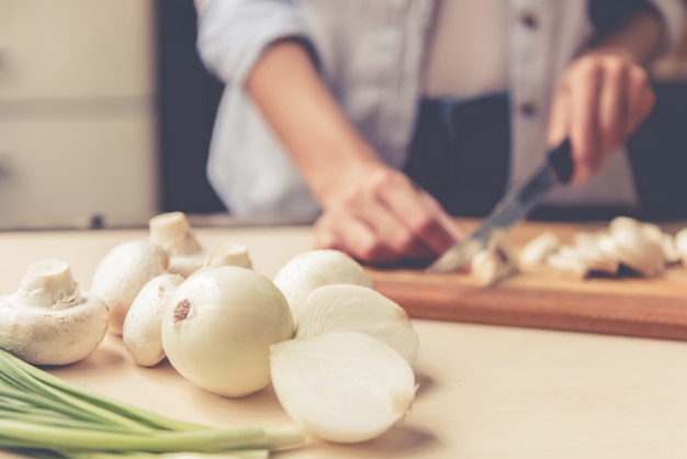 Comida na mesa da cozinha, a menina está cortando cogumelos