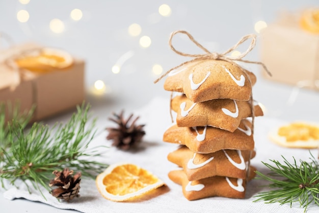 Comida navideña. Galletas de jengibre caseras, ramas de pino, piñas, naranjas secas. Luces del árbol de Navidad en el fondo.