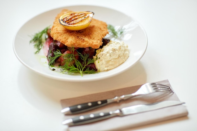 comida, nueva cocina nórdica, cena, culinaria, alta cocina y concepto de cocina - primer plano de filete de pescado en pan con salsa tártara y ensalada de tomate de remolacha horneada en el plato