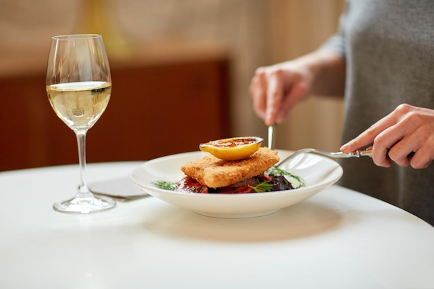 comida, nueva cocina nórdica y concepto de gente - mujer comiendo filete de pescado empanizado con remolacha al horno y ensalada de tomate con tenedor y cuchillo en una cafetería o restaurante