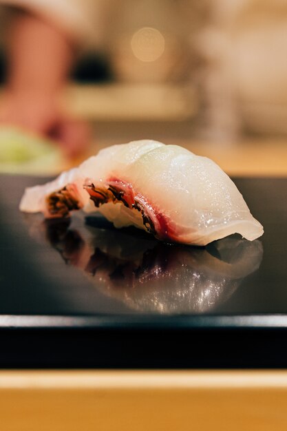 Comida Omakase japonesa: Cierre de Tai (pescado de dorada) Sushi servido en un plato negro brillante. Comida japonesa de lujo.