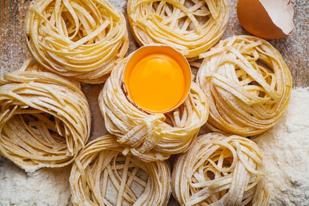 Comida de pasta fresca. Pasta italiana casera cocinada en una mesa de madera en un estilo rústico decorado con huevo y harina.