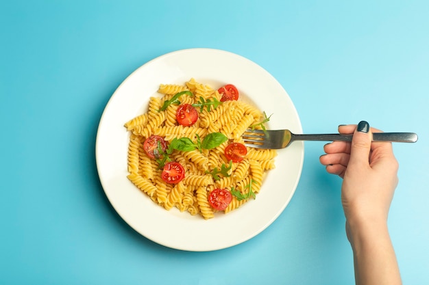 Comida de pasta sobre un fondo azul con manos femeninas. Pasta fusilli italiana con tomate y albahaca en un plato blanco.