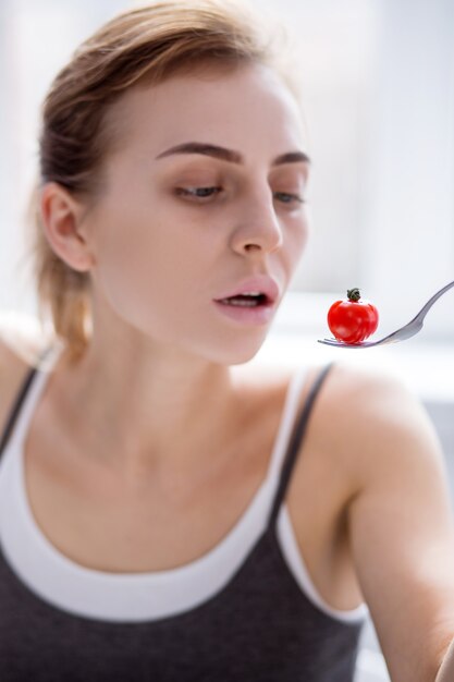 Comida pequeña. Enfoque selectivo de un pequeño tomate comido por una joven triste