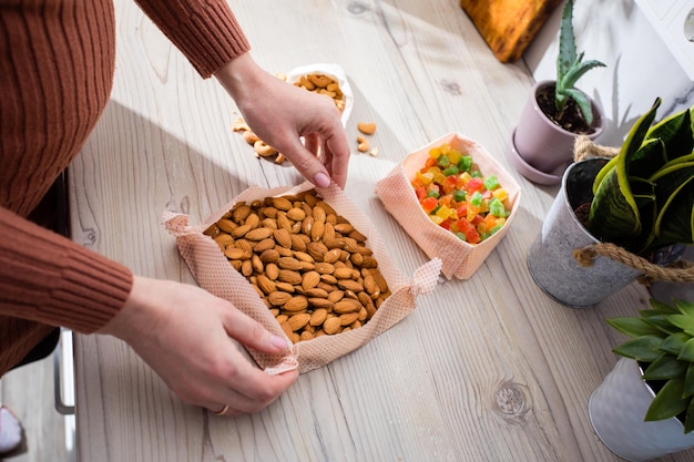 Comida de primer plano envuelta en tela de cera de abeja Merienda en caja hecha de origami de tela de envoltura de cera de abeja Mujer sostiene las nueces y frutos secos