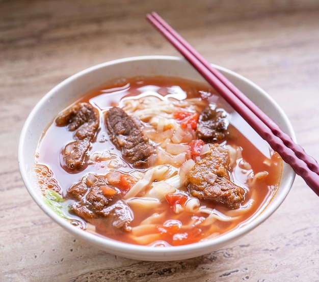 Comida de ramen de fideos de res con caldo de salsa de tomate en un tazón sobre una mesa de madera brillante famosa comida de estilo chino en Taiwán cerrar vista superior espacio de copia