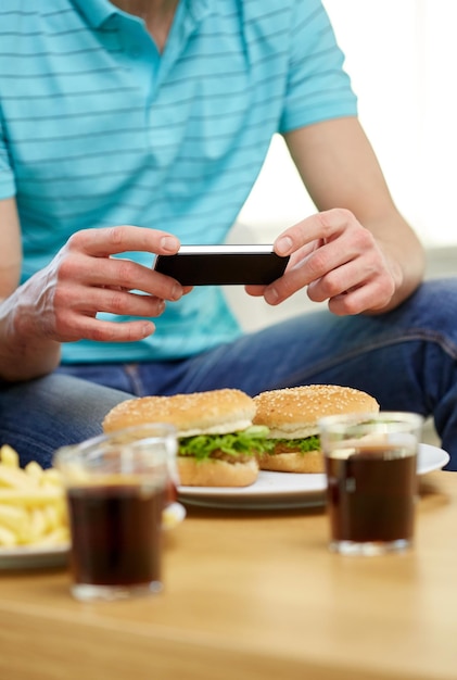 comida rápida, alimentación poco saludable, tecnología, gente y comida chatarra - cerca de un hombre con un smartphone fotografiando hamburguesas en casa