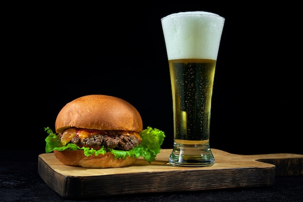 Comida rápida y cerveza light fría. Hamburguesa colocada sobre una tabla de madera en barra de bar con espacio de copia.