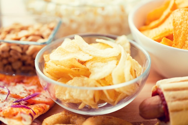 comida rápida, comida chatarra, cocina y concepto de alimentación: cierre de patatas fritas crujientes en un bol de vidrio y otros aperitivos